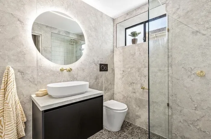 Elegant bathroom with a round backlit mirror, dark vanity and gold tapware