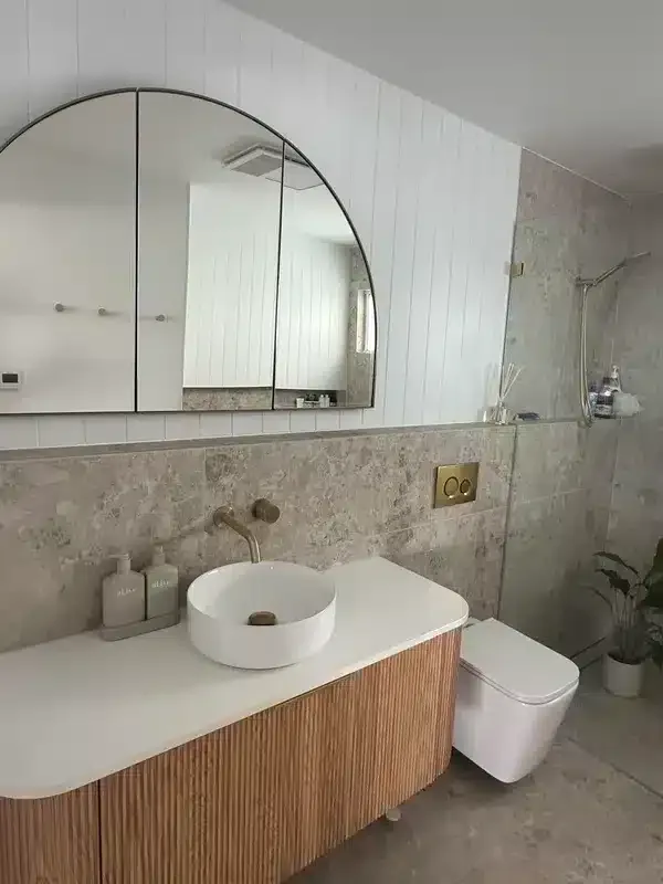 Arched-mirror vanity beside a wall-hung toilet in a light-filled ensuite