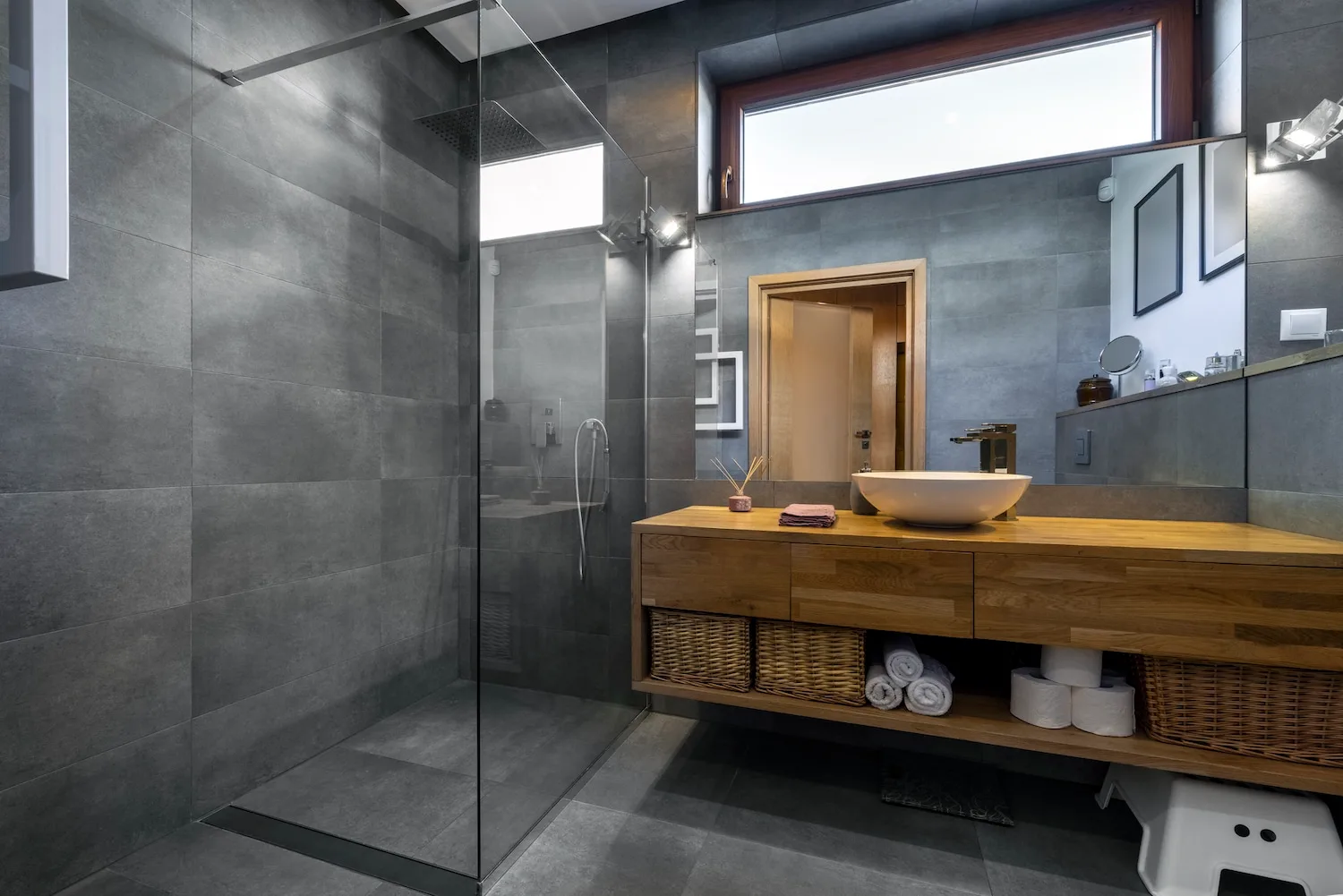 Charcoal-tiled walk-in shower beside a timber vanity with a vessel basin