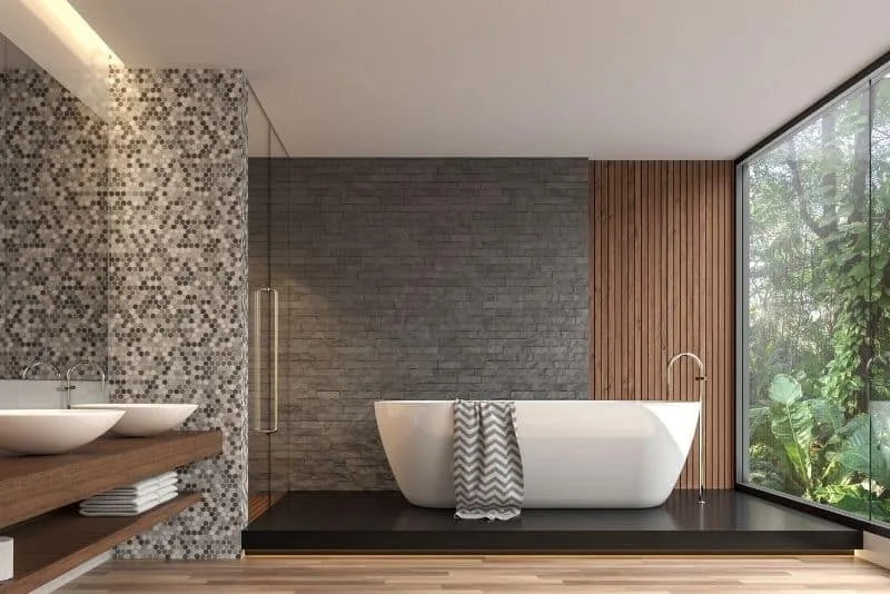 Dark stone luxury bathroom with a freestanding tub and jungle-view window