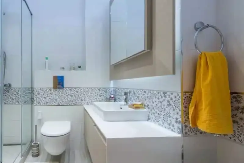 Small renovated toilet with floral tile trim and a yellow towel