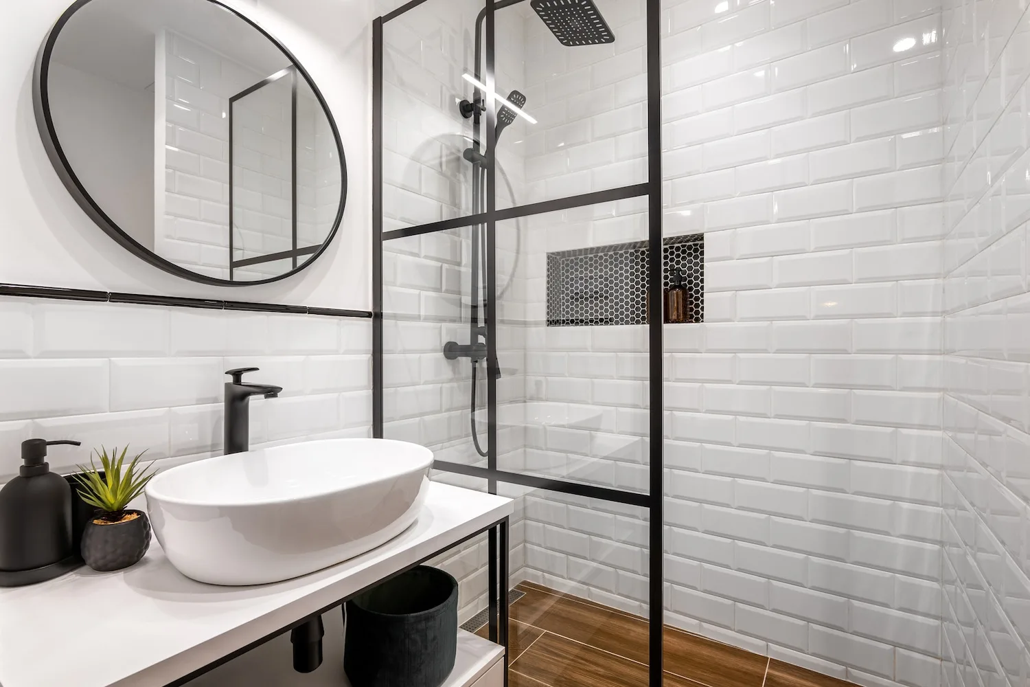 Black-framed glass shower with white subway tiles and a round mirror above a vessel sink