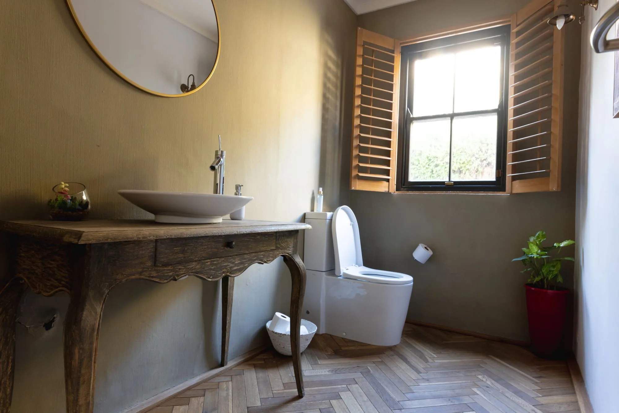 Standalone toilet beside a console vanity with a round mirror